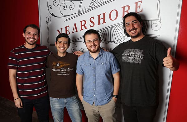 Four employees standing in front of the nearshore sign