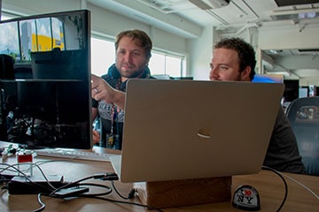 A laptop back with two employees looking at a screen behind it