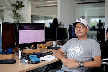 Senior Software Engineer with a First Factory t-shirt sitting in front of a computer, friendly smiling at the camera