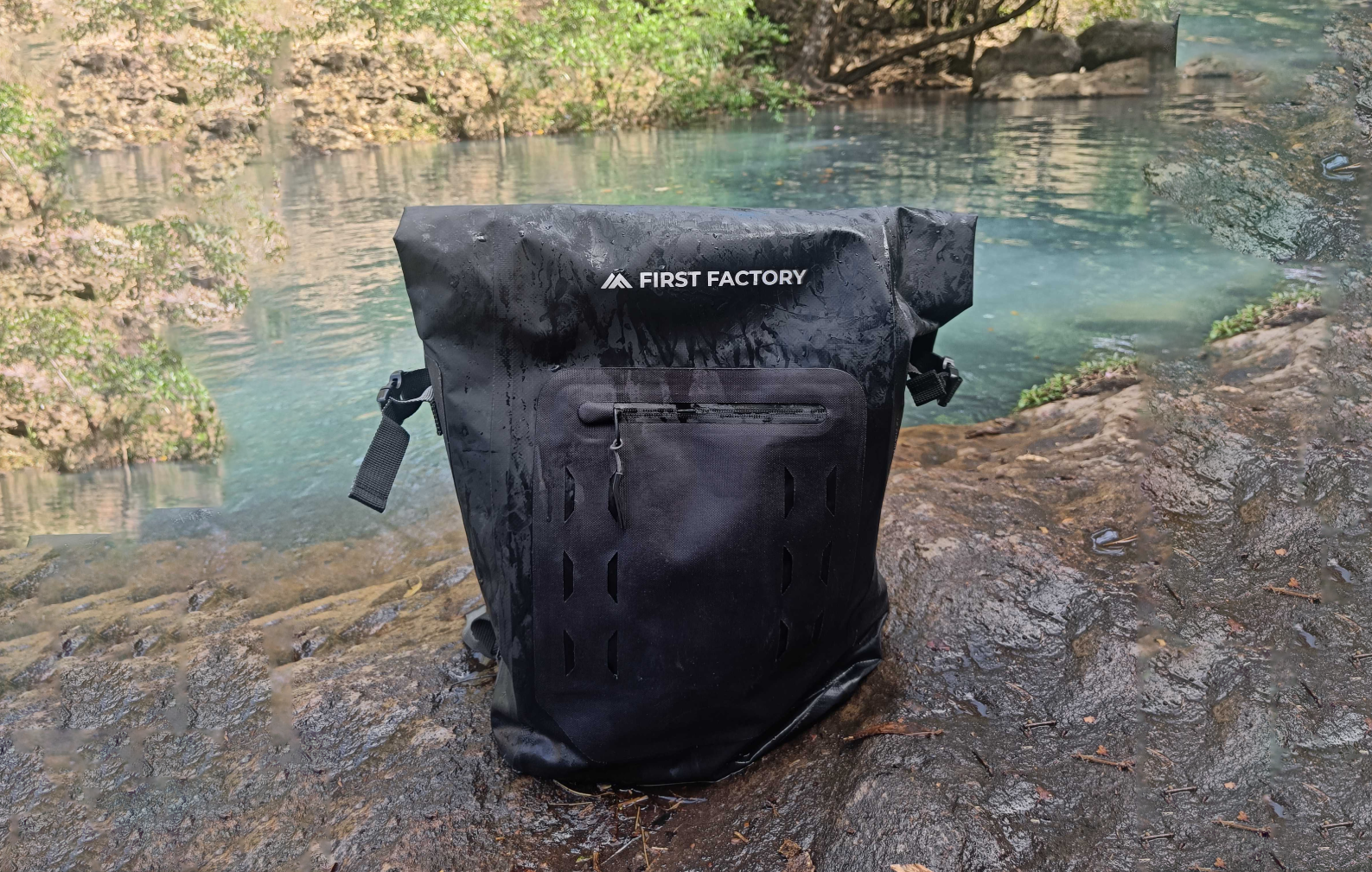 Black backpack branded with First Factory logo on rocky ground in one of Costa Rica's rivers